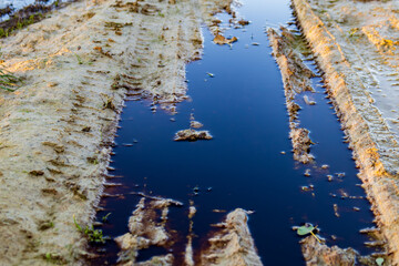 Dark, polluted water sits in a muddy area, showing the impact of waste and toxic materials on the environment
