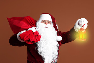 Santa Claus with red bag of Christmas gifts and lantern on brown background
