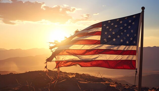 Tattered American flag waving at sunset, dramatic sky with orange hues and distant mountain valley. - Powered by Adobe