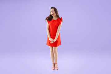 Beautiful woman in red dress posing on violet background