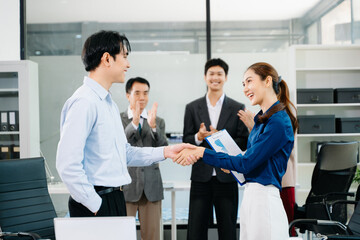 Asian business professionals shaking hands and celebrating success in a modern office, symbolizing teamwork, partnership