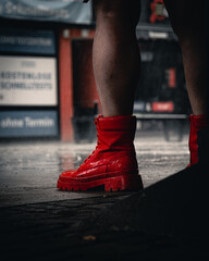 Bold red boots stand out in the rain on a city street during a cloudy day