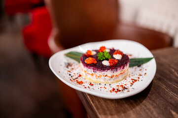 Shuba: traditional Russian layered salad of beets, vegetables, and herring topped with mayonnaise, garnished with red caviar and parsley on a white plate
