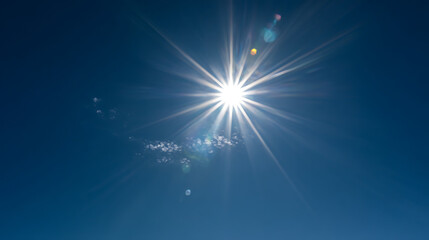 Brilliant sunburst shining through clear blue sky with wispy clouds bright light