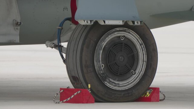 Close up view of a military jet wheel secured with red chocks on concrete surface
