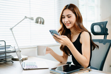 Happy businesswoman using smartphone and drinking coffee at laptop, symbolizing digital communication, modern lifestyle, and professional confidence.