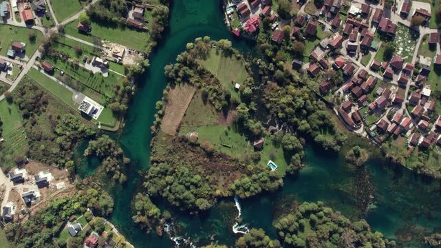 Drone footage showing a heart shaped curve of the Una River surrounded by greenery, fields and houses near Bihac, Bosnia and Herzegovina. Clear turquoise water and vibrant landscape seen from above.