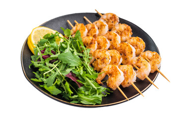 Grilled shrimp prawn skewers served on a black plate with fresh arugula salad and lemon. Healthy and light seafood meal on white background.