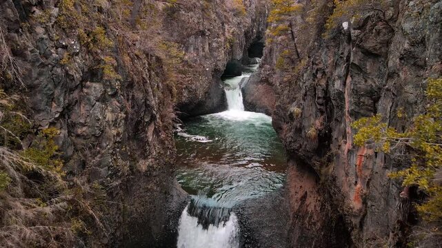 Backward drone aerial of multi-tiered waterfalls through narrow canyon, Siete Tazas National Park, &Ntilde;uble, Chile with rugged volcanic rock walls