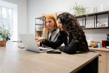 Two colleagues discuss a project over a laptop in a well-lit, contemporary kitchen workspace.