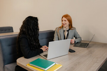 Two colleagues discuss ideas at a wooden table with laptops in a modern office.