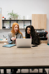 Two women work together on a laptop in a bright, modern workspace, planning a project.