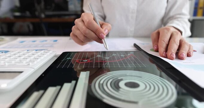 Businesswoman studies charts and diagrams on tablet and makes notes for future reference. Female studies data on digital device and makes comments