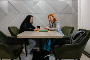 Two colleagues share notes and devices in a stylish, geometric-walled seating area.