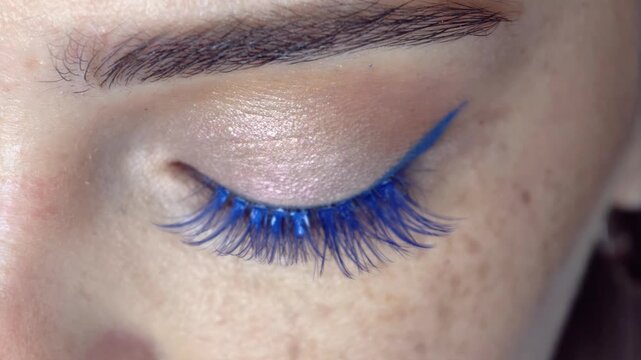 Makeup artist glues on false blue eyelashes. Close-up video of eyelash extension.