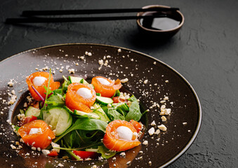 Salad with smoked salmon, cucumber, and cream on black plate