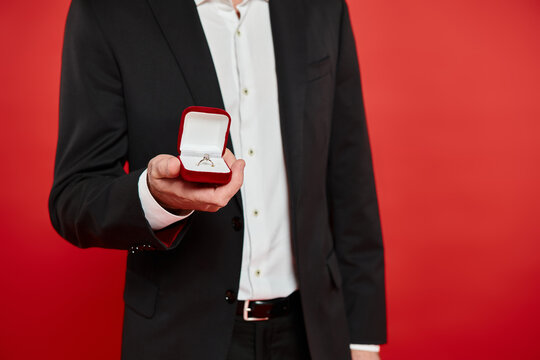 Romantic man in elegant suit presents engagement ring against vibrant red backdrop