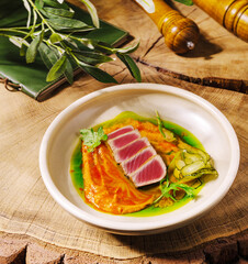 Gourmet seared tuna with colorful sauce and fresh herbs on wooden table