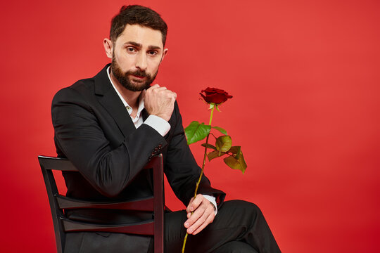 Man in a suit holding a rose on a vibrant red background for Valentines Day - Powered by Adobe