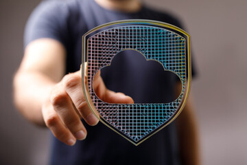 A hand touches a digital shield with a cloud symbol, representing data protection, security, and the concept of cloud computing.