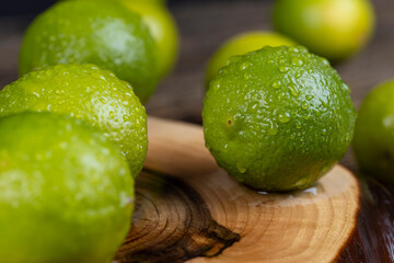 wet green citrus limes scattered on the wooden table in the kitchen, ripe and juicy lime fruits for cooking, green limes covered with drops of water