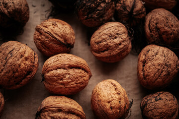 A rustic arrangement of whole walnuts scattered on a brown paper surface reveals natural textures and earthy tones. Soft lighting creates a warm, organic feel.