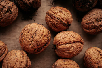 A rustic arrangement of whole walnuts scattered on a brown paper surface reveals natural textures and earthy tones. Soft lighting creates a warm, organic feel.