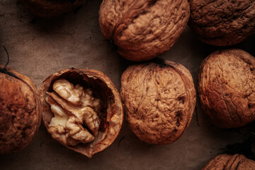 A detailed macro shot of several whole walnuts and one cracked open, revealing the kernel inside, placed on a textured surface. Earth tones, natural light.