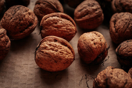 A rustic arrangement of whole walnuts scattered on a brown paper surface reveals natural textures and earthy tones. Soft lighting creates a warm, organic feel.