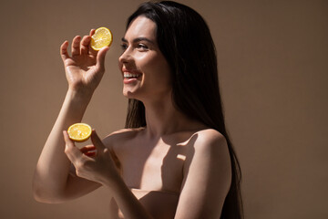 Young woman with long dark hair holds fresh lemon halves, smiling joyfully, illuminated by soft...