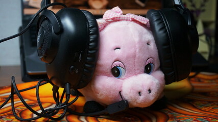 Pink pig toy wearing headphones with wires on the background of a blurred laptop