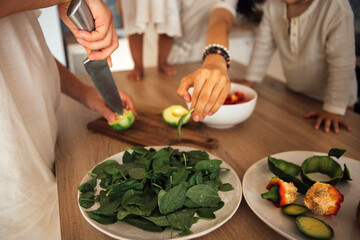 Hands of a woman chopping fresh vegetables on a wooden cutting board, surrounded by healthy ingredients, showcasing a vibrant cooking scene with family involvement and culinary creativity