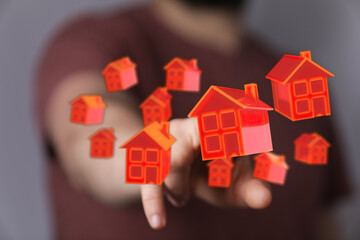 A person's finger pointing at floating holographic houses, representing homeownership, property investment, real estate dreams and future. Ideal