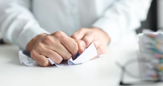 Office worker hand crumples paper sheet on desk. Worker rejects draft and  squeezes page preparing to drops waste into bin after stressful moment