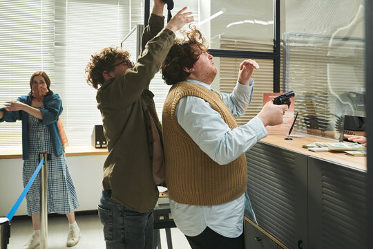 Brave young Caucasian man trying to stop bank robbery, revealing robbers face, taking off his mask, female crime partner in background