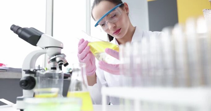 Woman lab technician wearing gloves investigates sample in flask by rack. Technician checks label and aligns vials preparing test under microscope - Powered by Adobe