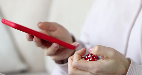 Person holding red smartphone scrolls feed with thumb sitting on sofa. Hand rotates fidget dice keeping idle play while important messages arrive - Powered by Adobe