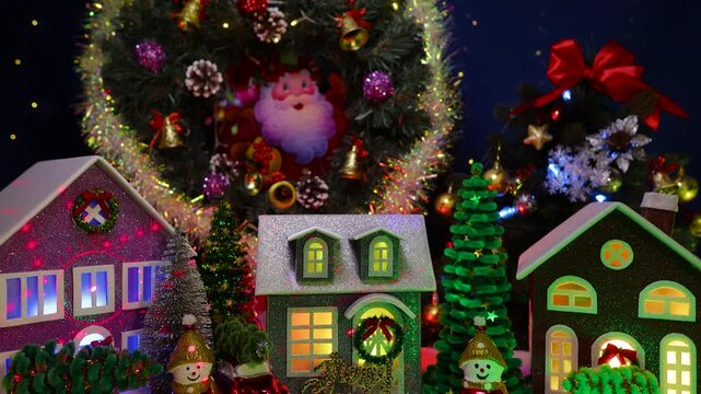 In the center of the Christmas village there is a gray house with letters in front against the backdrop of a large Christmas tree and a Christmas wreath