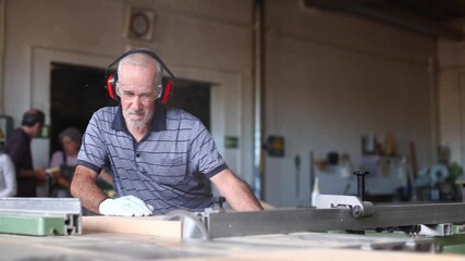 Senior carpenter cutting wood plank with circular saw