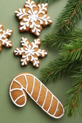 Tasty gingerbread cookies and fir branches on green background, flat lay. Christmas treat