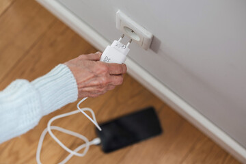 Close-up of senior woman inserting a power plug into a socket to charge her phone
