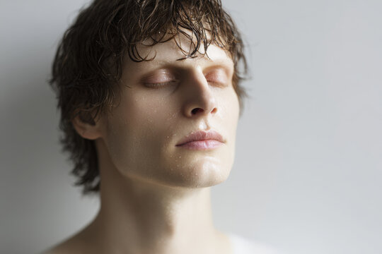 young man with wet eyelashes and heavy breath stands against clean solid background