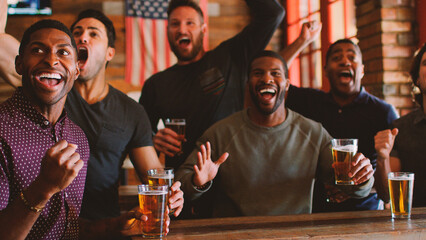 Group Of Male Friends Celebrating Whilst Watching Game On Screen In Sports Bar