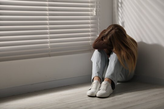 Depressed teenage girl near window at home, space for text