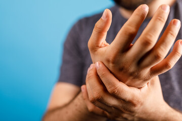 Fototapeta premium Close-up of a man holding his painful wrist, shows discomfort and medical concern, potential for injury and treatment, background blue.