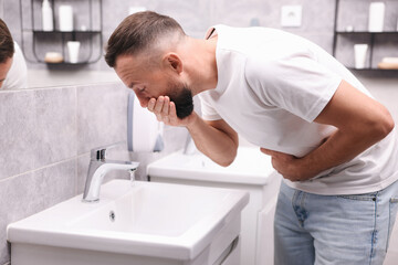 Obraz premium Man suffering from stomach ache and nausea over sink in bathroom
