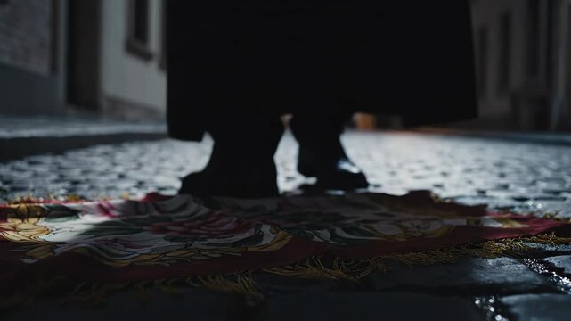 Fancy scarf with floral pattern lying on a wet cobblestone street at night as a person walks away, suggesting themes of loss, abandonment, and mystery in an urban setting