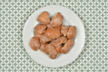 A white plate heaped with various irregularly shaped, unglazed gingerbread cookies is placed centrally on a green and white geometric patterned tablecloth