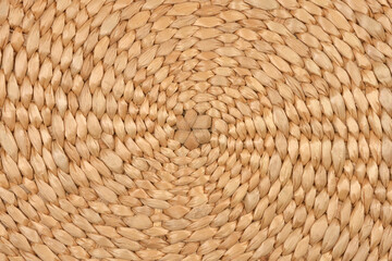 A full-frame, detailed close-up of a natural light brown woven texture with a central circular pattern of tightly braided plant fibers
