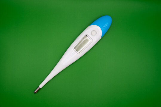 Close-up of a white and blue digital thermometer on bright green background. Health and medical concept representing temperature measurement and wellness care.